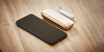 An IQOS DUO kit and a mobile on a wooden surface