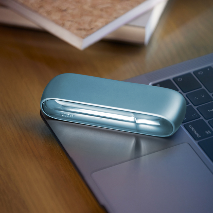 IQOS Heated tobacco device in turquoise color on a laptop.