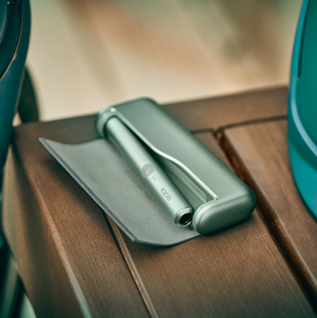 A moss green IQOS ILUMA device and charger resting on a table