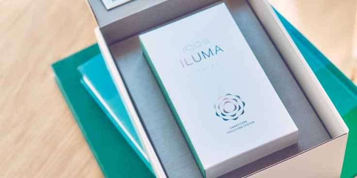 An open IQOS ILUMA box on the pile of books.