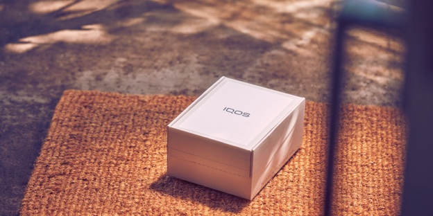 An unopened IQOS device box on a rug.