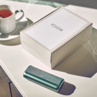 Jade Green zeleni IQOS ILUMA PRIME džepni punjač i IQOS kutija na stolu.
