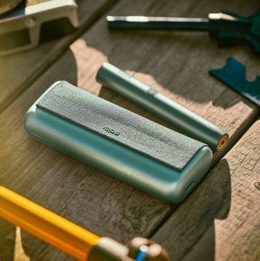 Jade Green zeleni IQOS ILUMA PRIME držač i džepni punjač na drvenom stolu.