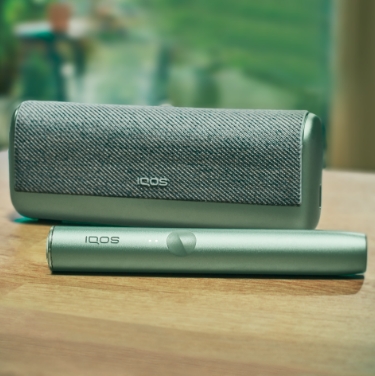 A Jade Green IQOS ILUMA PRIME Holder and Pocket Charger on a wooden table.