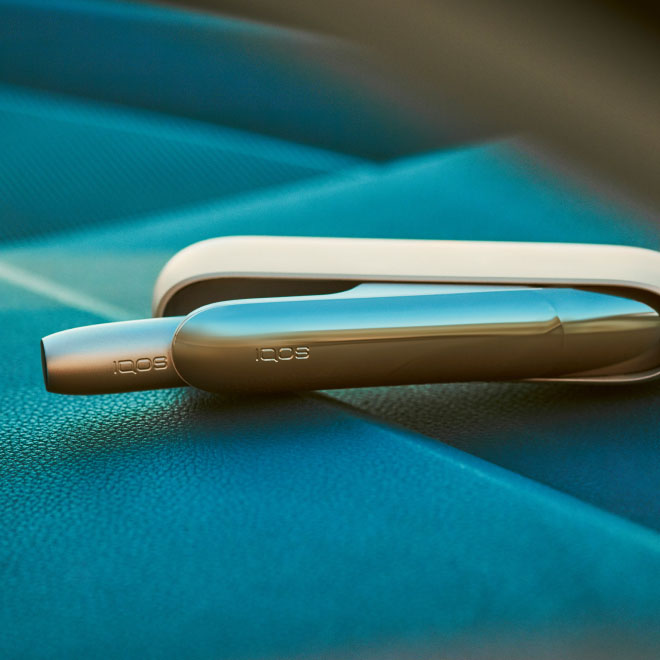IQOS device and its charger on a blue background