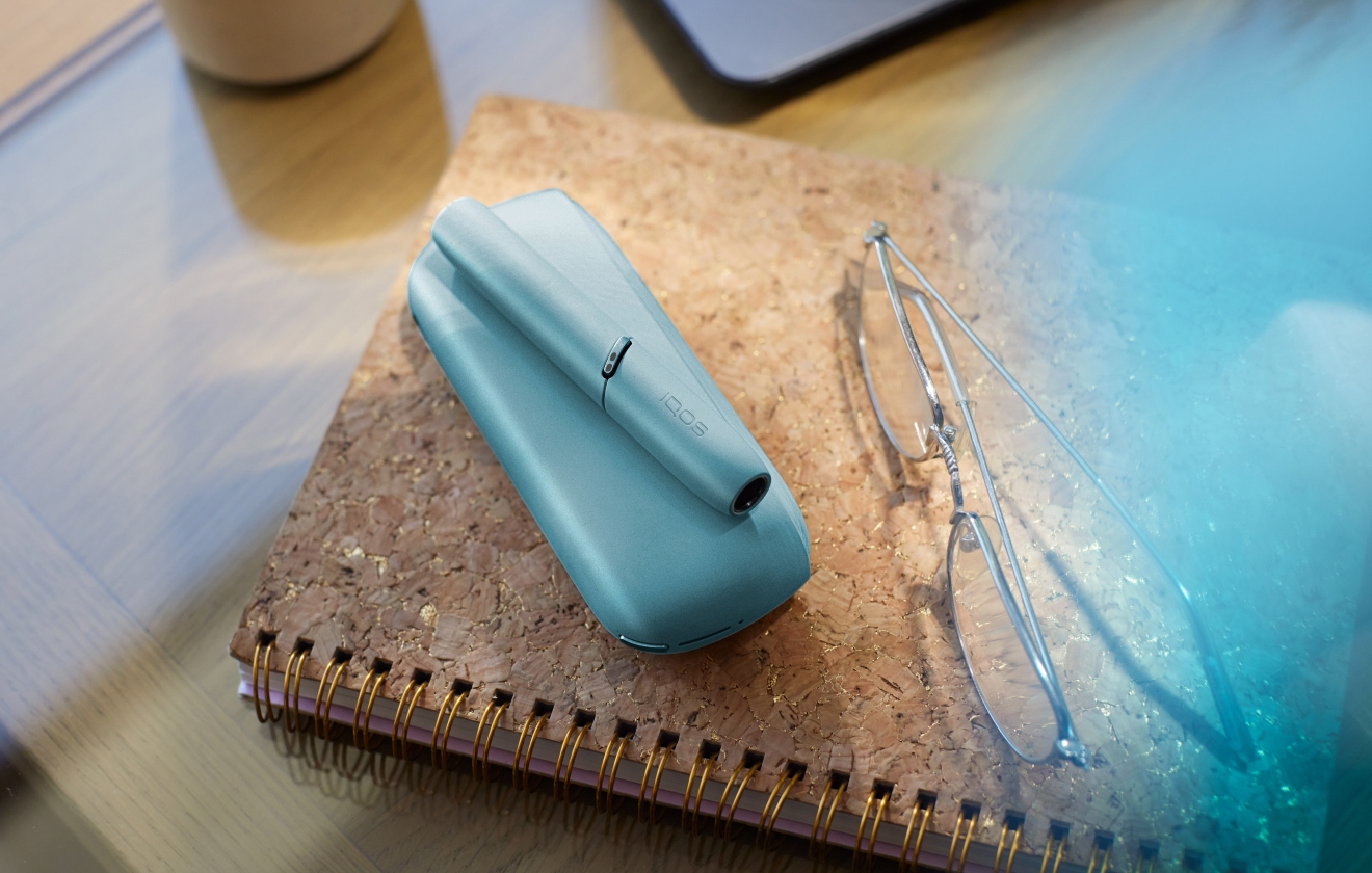 Hands holding IQOS Originals Duo heated tobacco holder and pocket charger in turquoise color.