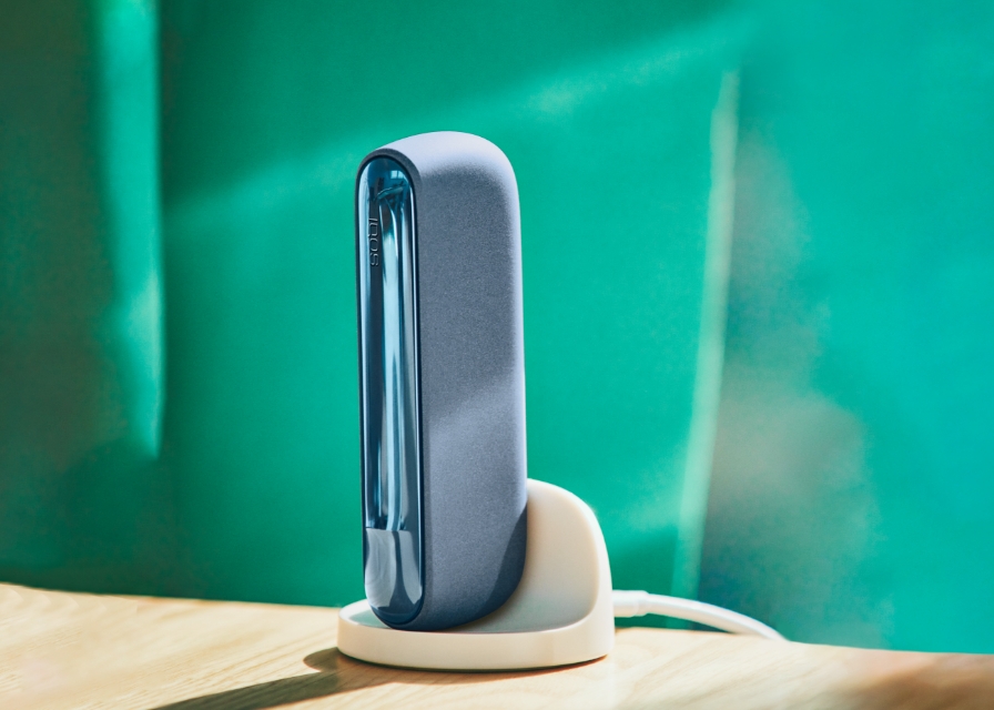 A mid azure blue IQOS ILUMA holder sits on the table.