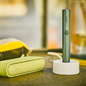 IQOS ILUMA držač u stanici za napajanje pokraj džepnog punjača na stolu.