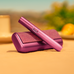 Garnet Red IQOS ILUMA i PRIME device above its charger, on a table outside