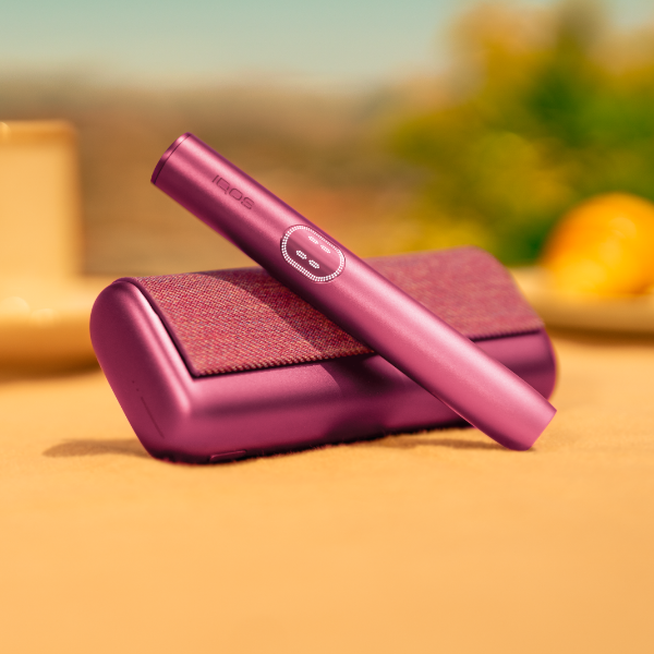 Garnet Red IQOS ILUMA i PRIME device above its charger, on a table outside