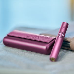 Držač IQOS ILUMA i PRIME uređaja u bordo Garnet Red boji pokraj džepnog punjača