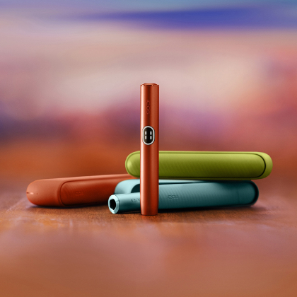Red IQOS ILUMA i device standing in front of three different coulours chargers