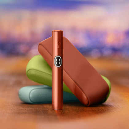Red IQOS ILUMA i device standing in front of three different coulours chargers