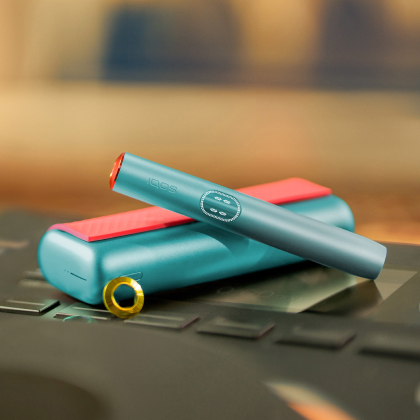 Blue IQOS ILUMA i PRIME device above its charger, customized with wrap and rings
