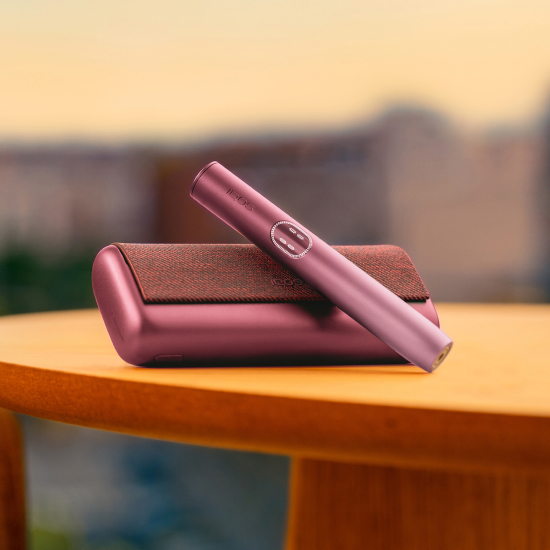 Garnet Red IQOS ILUMA i PRIME device above its charger, on a table