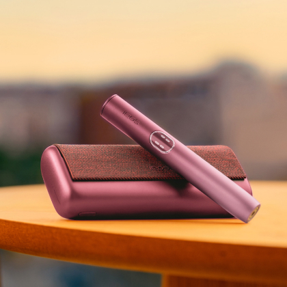 Garnet Red IQOS ILUMA i PRIME device above its charger, on a table