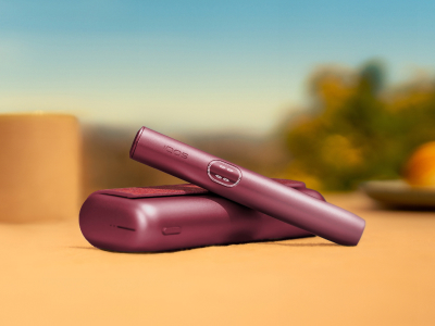 Garnet Red IQOS ILUMA i PRIME device above its charger, on a table outside