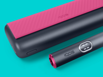 Red and black IQOS ILUMA i PRIME device and its charger on a light turquoise background