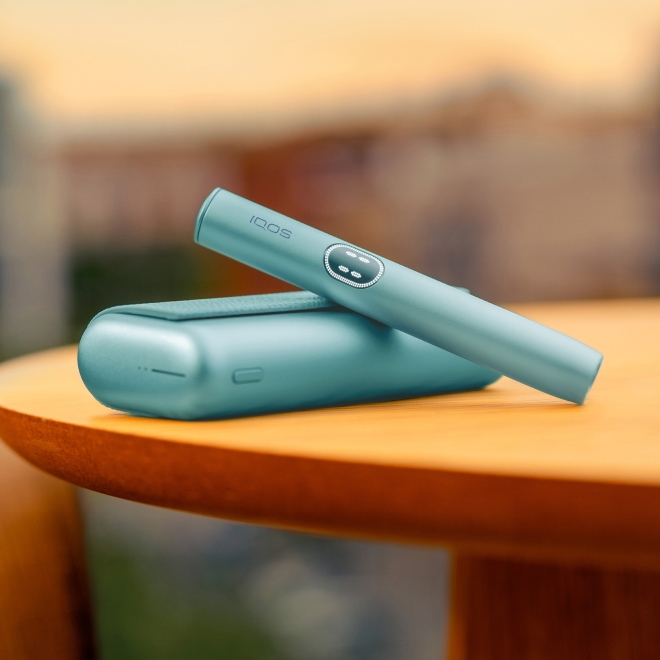 Blue IQOS ILUMA i PRIME device above its charger, on a table