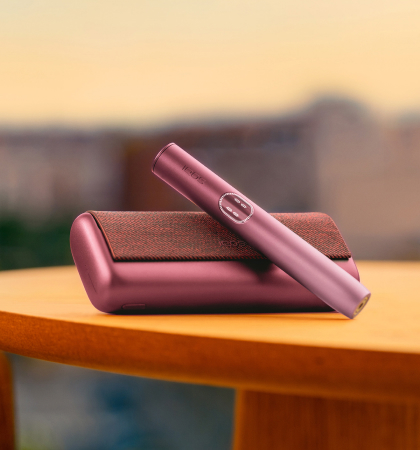 Garnet Red IQOS ILUMA i PRIME device above its charger, on a table near a couch