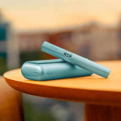 Blue IQOS ILUMA i PRIME device above its charger, on a table