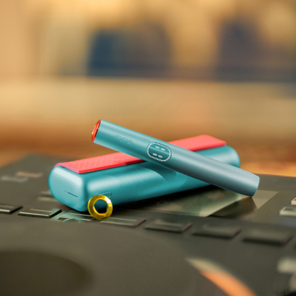 Blue IQOS ILUMA i PRIME device above its charger, customized with wrap and rings
