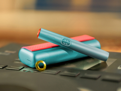 Blue IQOS ILUMA i PRIME device above its charger, customized with wrap and rings