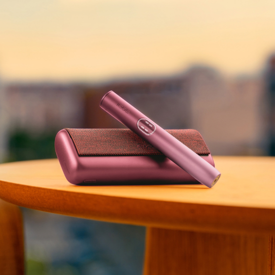 Garnet Red IQOS ILUMA i PRIME device above its charger, on a table