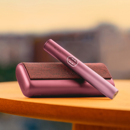 Garnet Red IQOS ILUMA i PRIME device above its charger, on a table