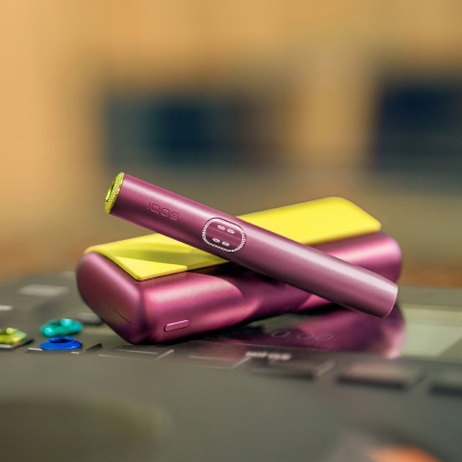 Breeze Blue IQOS ILUMA i PRIME device above its charger, with red background