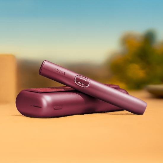 Garnet Red IQOS ILUMA i PRIME device above its charger, on a table outside