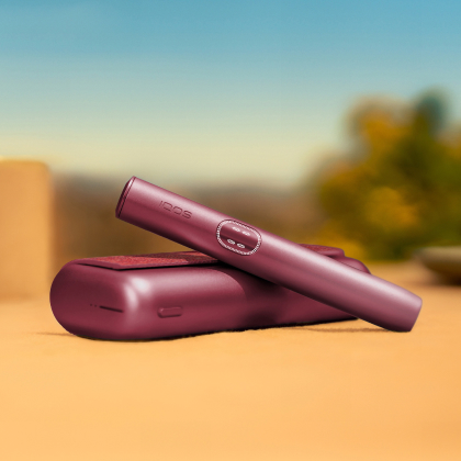 Garnet Red IQOS ILUMA i PRIME device above its charger, on a table outside
