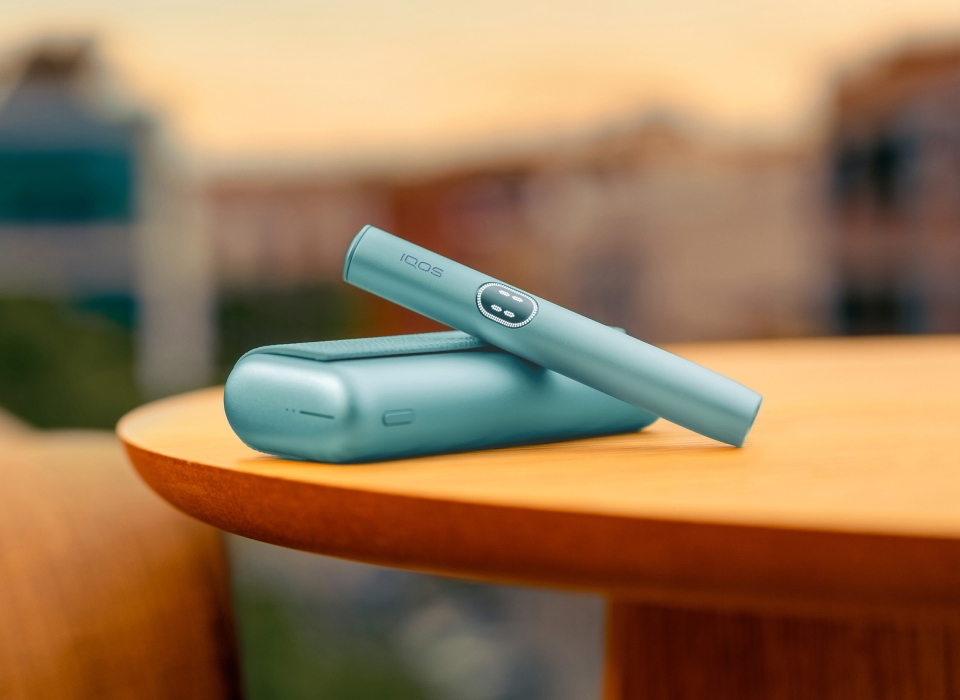 Blue IQOS ILUMA i PRIME device above its charger, on a table
