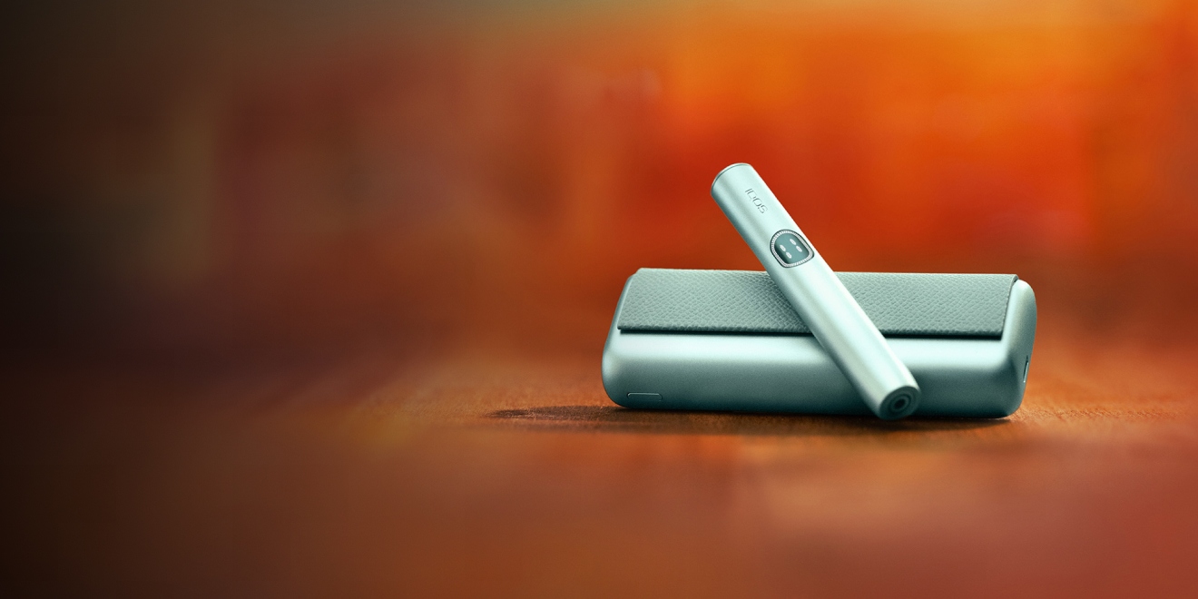 Breeze Blue IQOS ILUMA i PRIME device and its charger on an orange background