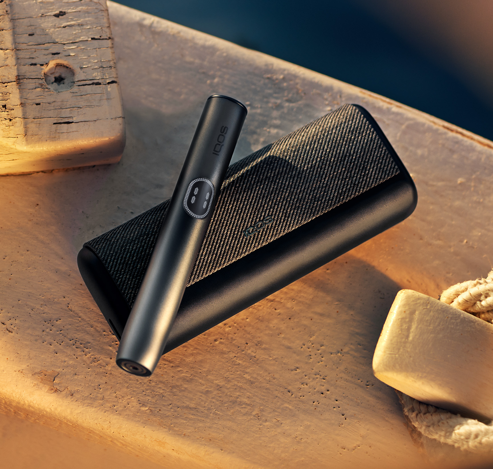 Midnight Black IQOS ILUMA i PRIME device with holder on top of it, on a wooden background