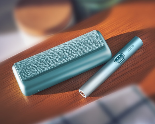 Blue IQOS ILUMA i PRIME device in next to its charger, on a wooden shelf