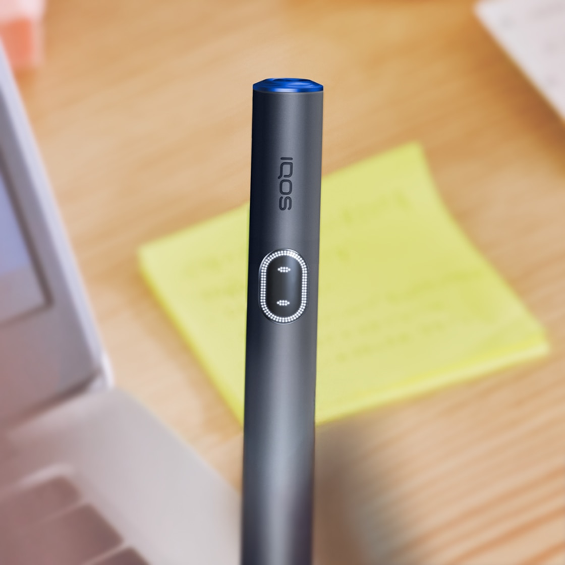 Držač IQOS ILUMA i PRIME uređaja u crnoj Midnight Black ispred samoljepivog papirića na stolu