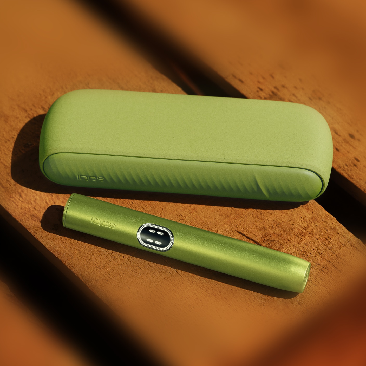 Green IQOS ILUMA i device next to its charger, on a wooden background