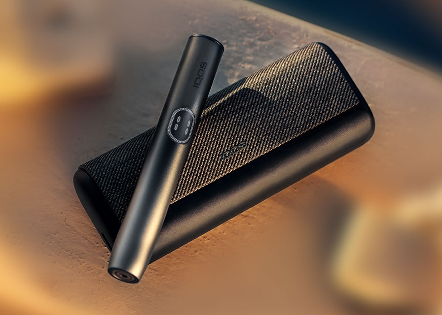 Black IQOS ILUMA i PRIME device above its charger, on a wooden background
