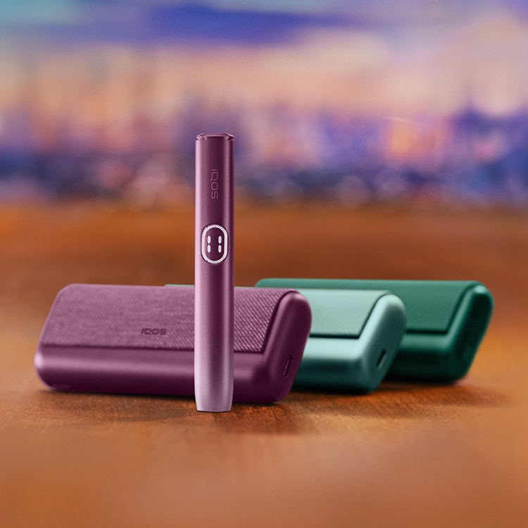 Držač IQOS ILUMA i PRIME uređaja u bordo Garnet Red boji stoji uspravno ispred 3 džepna punjača u različitim bojama