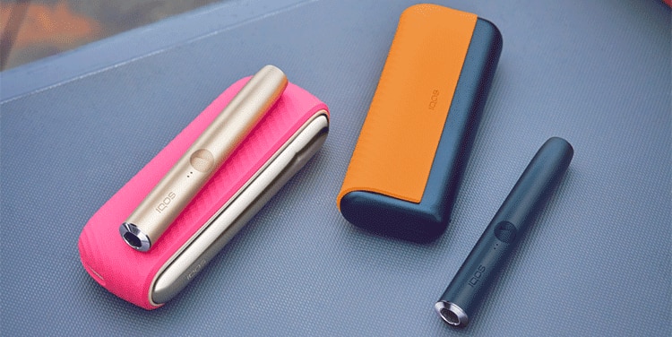 IQOS ILUMA device next to IQOS ILUMA PRIME device and its charger, with accessories in different colors