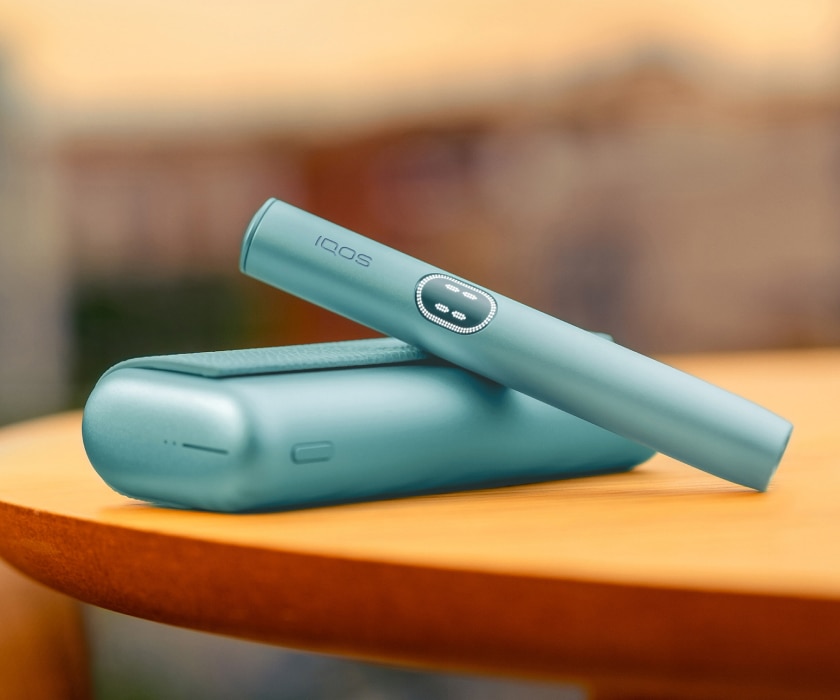 Blue IQOS ILUMA i PRIME device above its charger, on a table