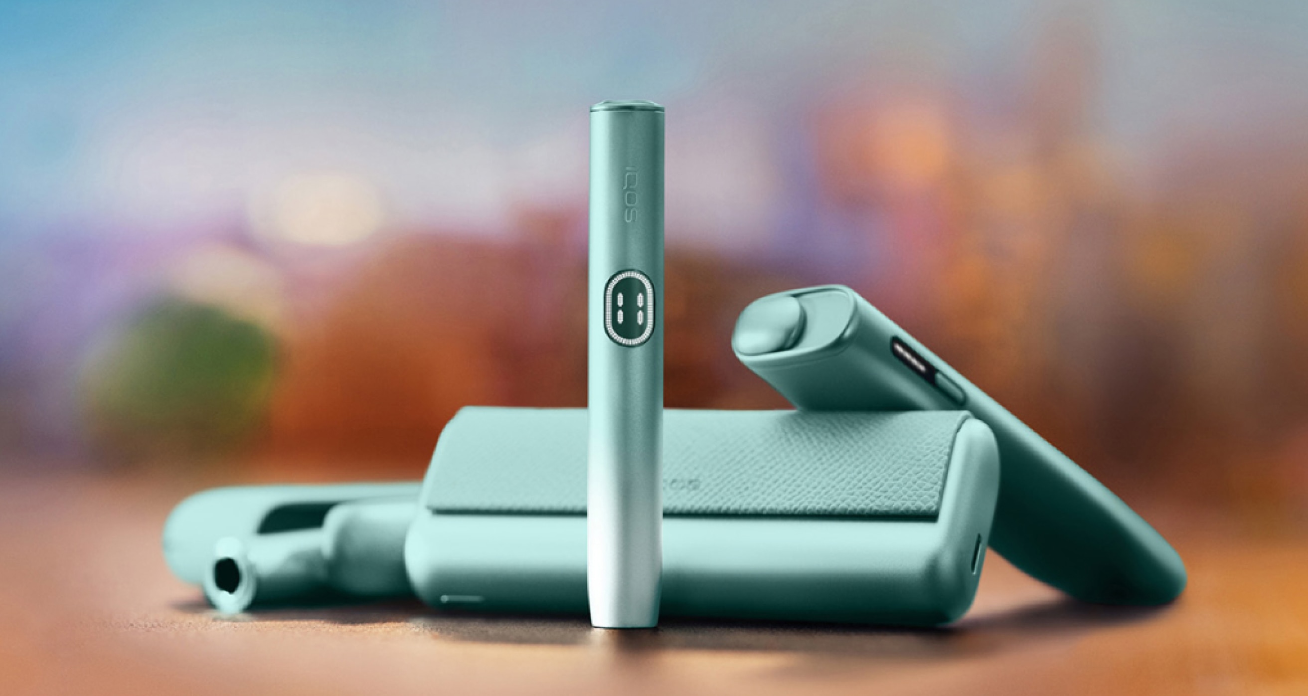 Tri IQOS ILUMA i uređaja jedan pokraj drugog, na mutnoj narančastoj pozadini.